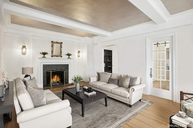 living room featuring a brick fireplace, beamed ceiling, and wood finished floors