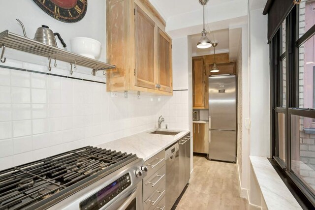 kitchen featuring light wood finished floors, decorative backsplash, appliances with stainless steel finishes, decorative light fixtures, and a sink