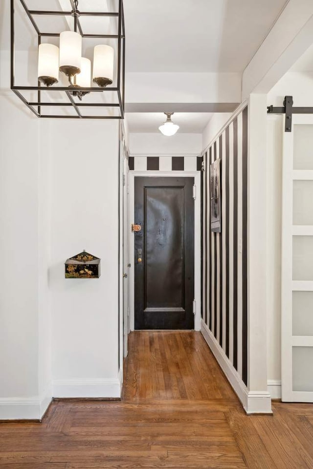 corridor with a notable chandelier, a barn door, wood finished floors, and baseboards