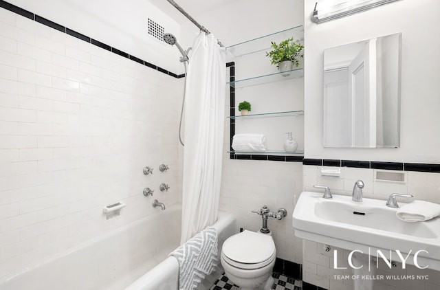 bathroom with toilet, shower / bathtub combination with curtain, a sink, and tile walls