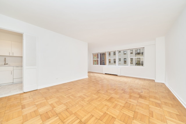 spare room with baseboards, a sink, and radiator heating unit