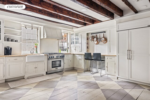 kitchen with a sink, high end range, open shelves, glass insert cabinets, and custom range hood