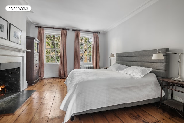 bedroom featuring ornamental molding, a warm lit fireplace, radiator heating unit, and wood finished floors