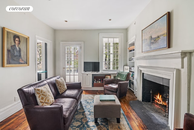 living area with a warm lit fireplace, baseboards, visible vents, and dark wood-type flooring