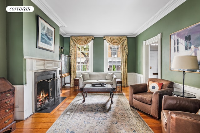 living area with a fireplace with flush hearth, a wainscoted wall, crown molding, and wood finished floors