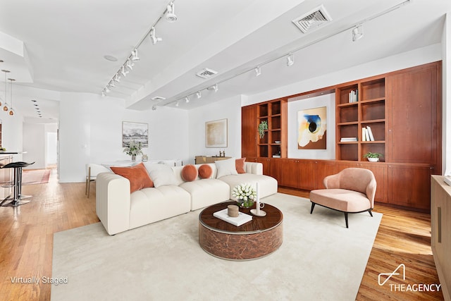 living room with light wood-style flooring, built in shelves, visible vents, and track lighting