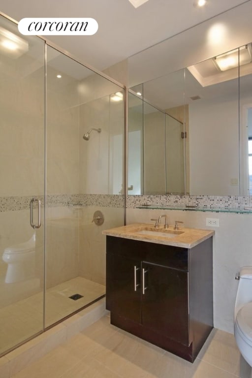 bathroom featuring tile patterned flooring, toilet, a shower with shower door, tile walls, and vanity