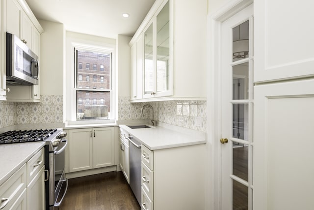 kitchen featuring light countertops, a sink, backsplash, appliances with stainless steel finishes, and dark wood-style floors