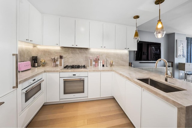 kitchen with white oven, white cabinetry, kitchen peninsula, and sink