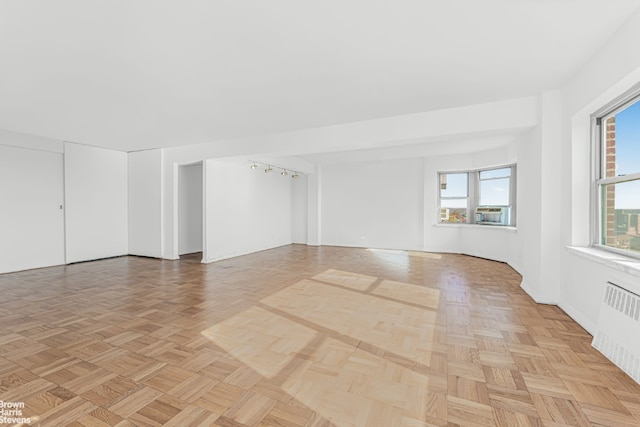 spare room featuring radiator, light parquet floors, and a healthy amount of sunlight