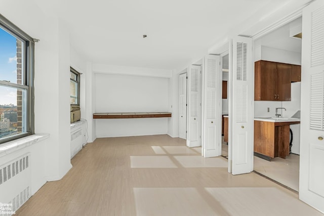 corridor with a wealth of natural light, radiator heating unit, and light hardwood / wood-style flooring