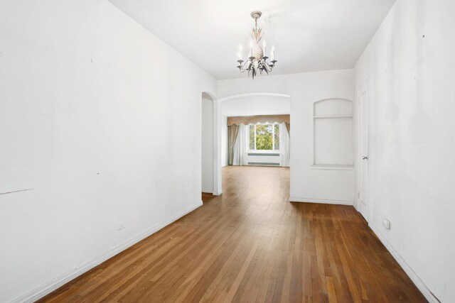 interior space with built in shelves, wood-type flooring, and an inviting chandelier