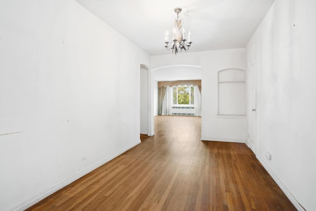 unfurnished dining area featuring arched walkways, wood finished floors, baseboards, built in features, and an inviting chandelier