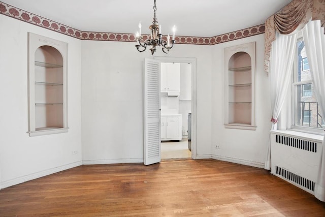 unfurnished dining area featuring baseboards, built in features, radiator, wood finished floors, and an inviting chandelier