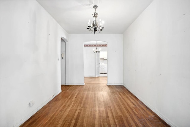 unfurnished dining area with baseboards, arched walkways, a notable chandelier, and wood finished floors