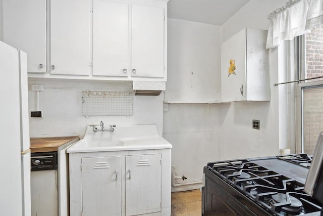 kitchen featuring gas range oven, light countertops, freestanding refrigerator, white cabinets, and a sink