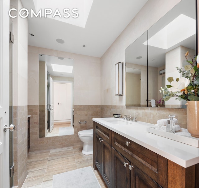 bathroom with toilet, tile walls, a skylight, wainscoting, and vanity