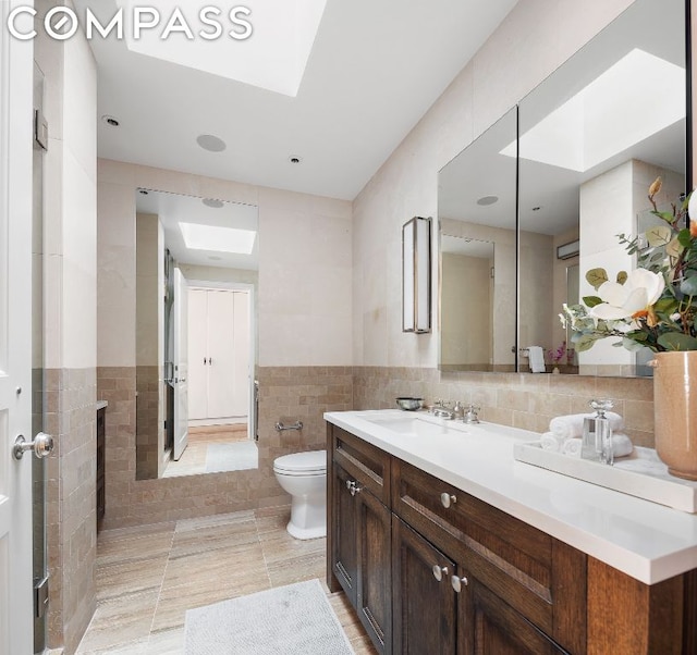 bathroom with vanity, toilet, a skylight, and tile walls