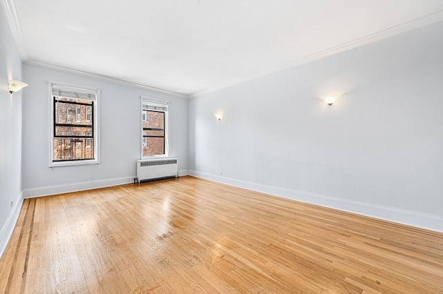 spare room featuring radiator heating unit, ornamental molding, light wood-type flooring, and baseboards