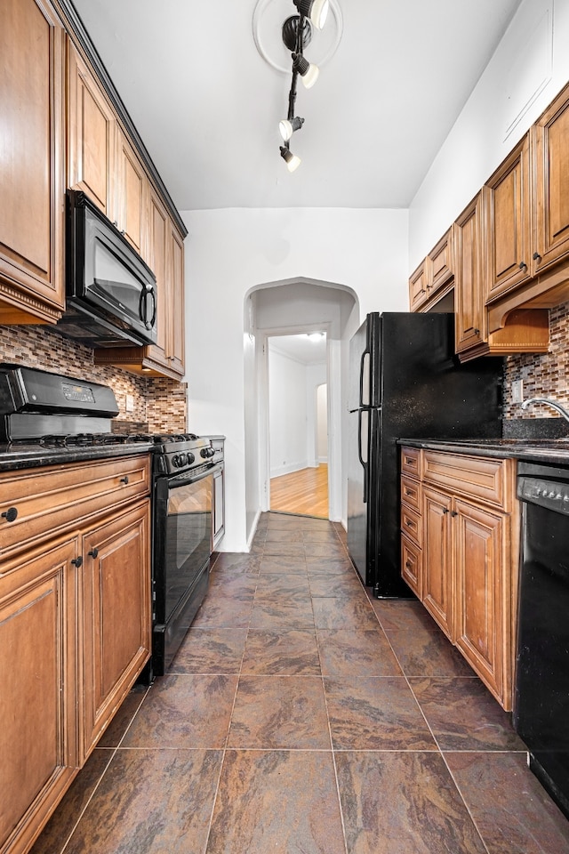 kitchen with black appliances, dark countertops, arched walkways, and backsplash
