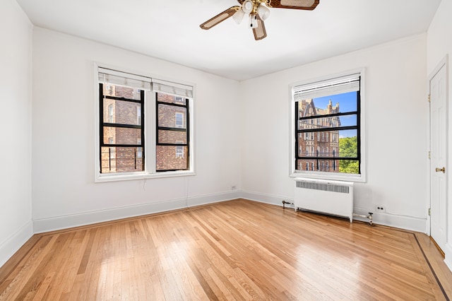 empty room featuring a ceiling fan, wood-type flooring, baseboards, and radiator heating unit