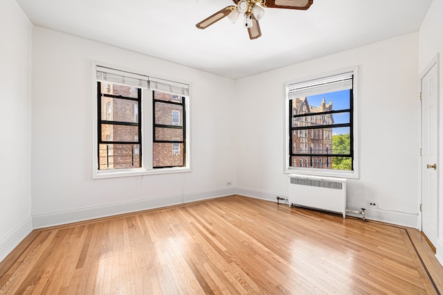 unfurnished room featuring radiator heating unit, light wood-type flooring, a ceiling fan, and baseboards