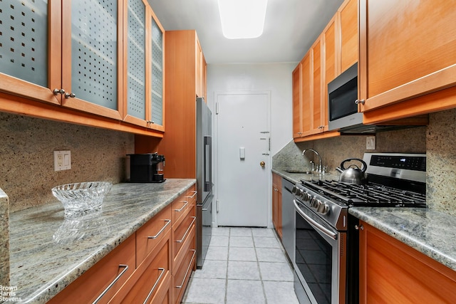 kitchen with a sink, stainless steel appliances, light tile patterned flooring, and brown cabinetry