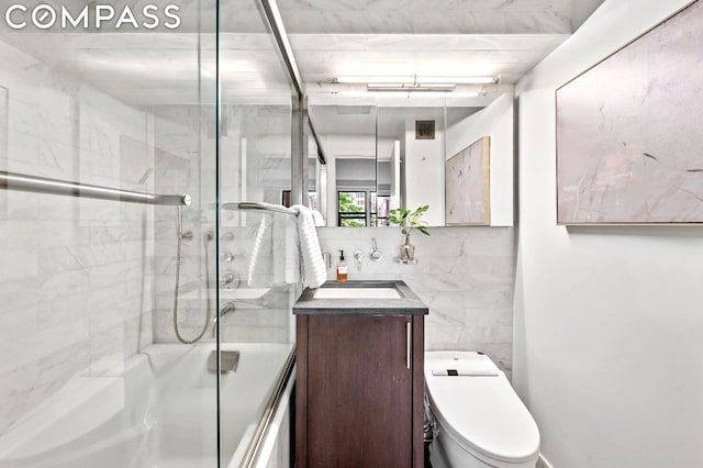 full bathroom featuring tile walls, enclosed tub / shower combo, vanity, and toilet