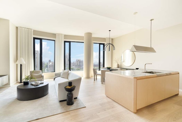 kitchen with sink, light hardwood / wood-style flooring, hanging light fixtures, a center island with sink, and light brown cabinets