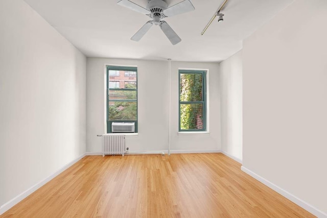 unfurnished room with hardwood / wood-style floors, radiator, track lighting, cooling unit, and ceiling fan