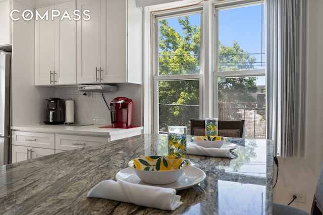 kitchen featuring tasteful backsplash, white cabinetry, freestanding refrigerator, and stone counters