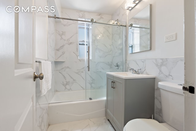 bathroom with toilet, tile walls, vanity, marble finish flooring, and bath / shower combo with glass door