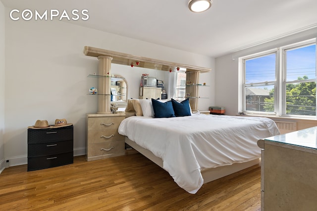 bedroom with multiple windows, light wood-style floors, and baseboards