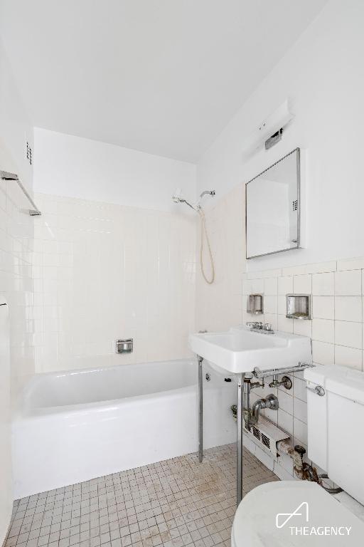 bathroom with toilet, shower / bathtub combination, tile patterned floors, and tile walls