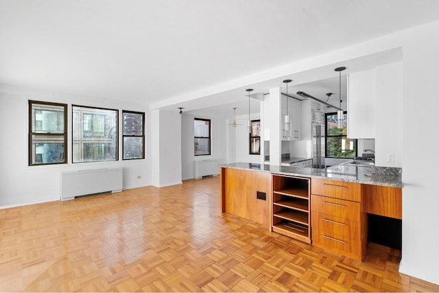 kitchen featuring light stone countertops, radiator heating unit, light parquet flooring, sink, and hanging light fixtures