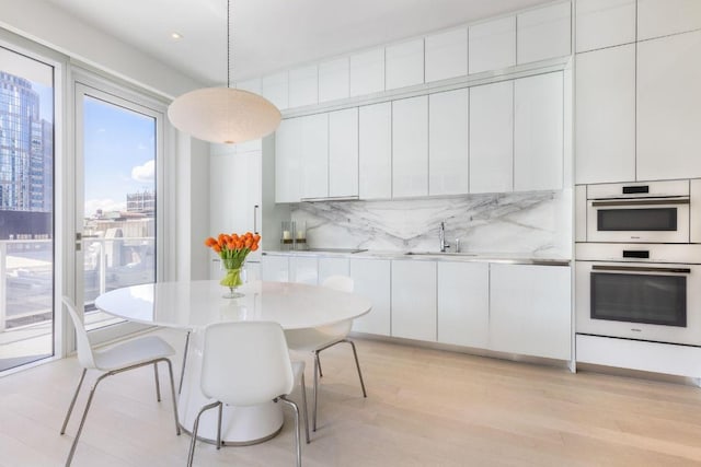 kitchen with sink, double oven, tasteful backsplash, white cabinets, and decorative light fixtures