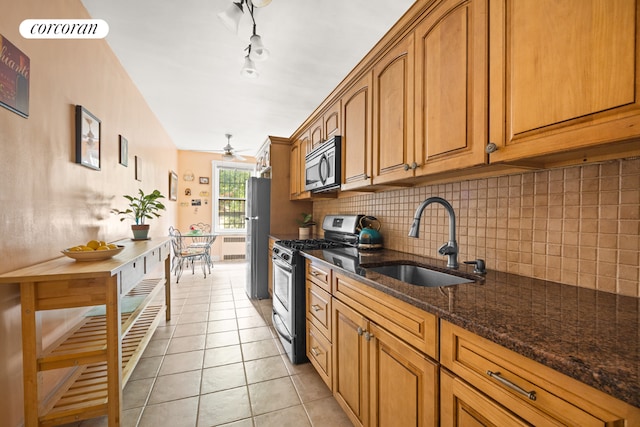 kitchen featuring light tile patterned floors, stainless steel appliances, decorative backsplash, dark stone counters, and sink