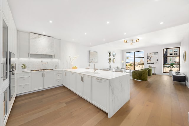 kitchen with kitchen peninsula, sink, stainless steel gas cooktop, light wood-type flooring, and white cabinets