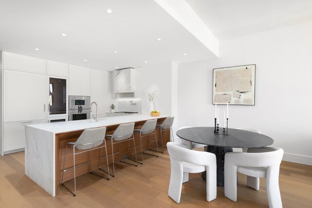 kitchen featuring white cabinetry, sink, light wood-type flooring, gas cooktop, and a breakfast bar area