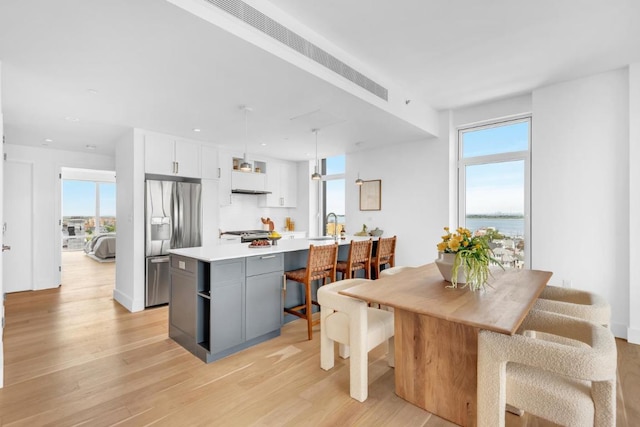 kitchen with gray cabinetry, a water view, hanging light fixtures, stainless steel appliances, and white cabinets