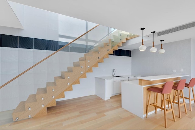 bar featuring white cabinetry, hanging light fixtures, light hardwood / wood-style flooring, and sink