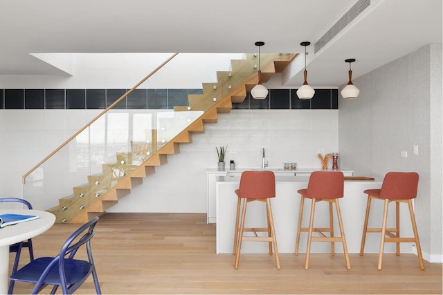 bar with hanging light fixtures, sink, white cabinets, and light wood-type flooring