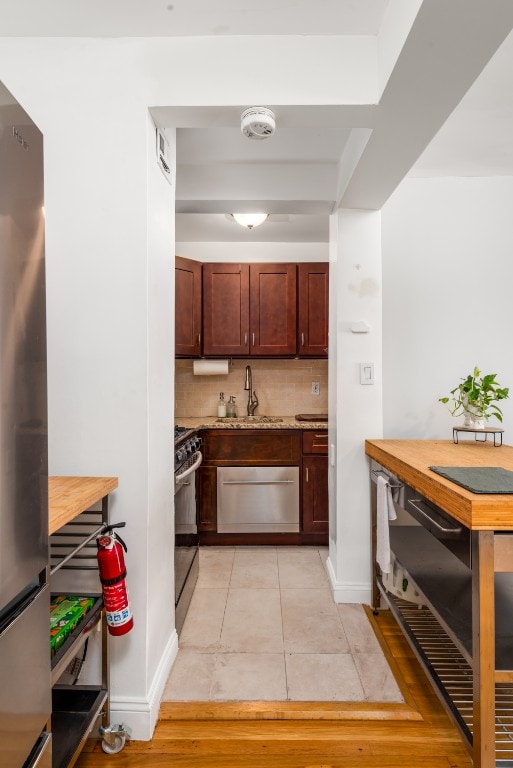 kitchen with light tile patterned floors, freestanding refrigerator, a sink, range with gas cooktop, and tasteful backsplash