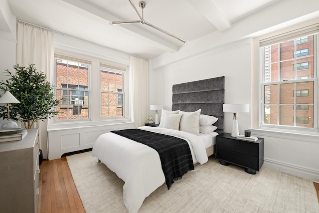 bedroom featuring light wood-type flooring, beam ceiling, and multiple windows