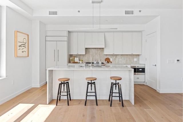 kitchen with an island with sink, tasteful backsplash, and white cabinetry