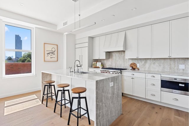 kitchen with custom exhaust hood, an island with sink, and white cabinets