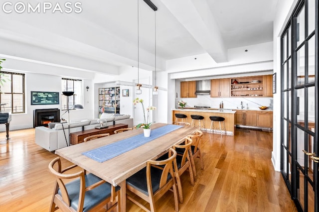 dining space with light hardwood / wood-style floors, sink, and beamed ceiling