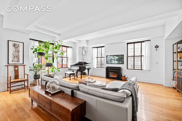 living room featuring light wood-type flooring, a warm lit fireplace, plenty of natural light, and baseboards