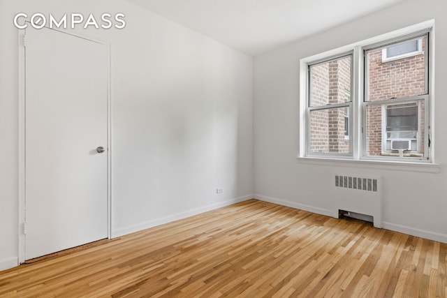 empty room with radiator, light wood-style flooring, and baseboards