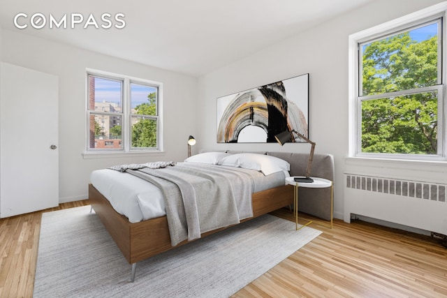 bedroom featuring multiple windows, light wood-style flooring, and radiator